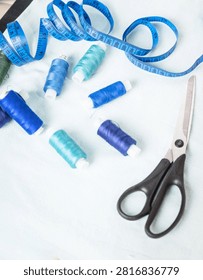 Scissors and blue thread spools on white surface, sewing, tools,