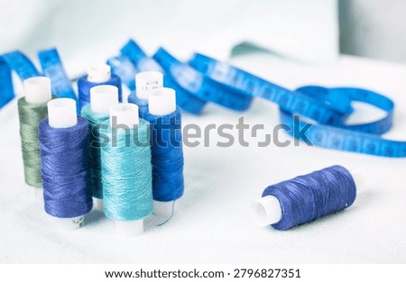 Scissors and blue thread spools on white surface, sewing, tools,