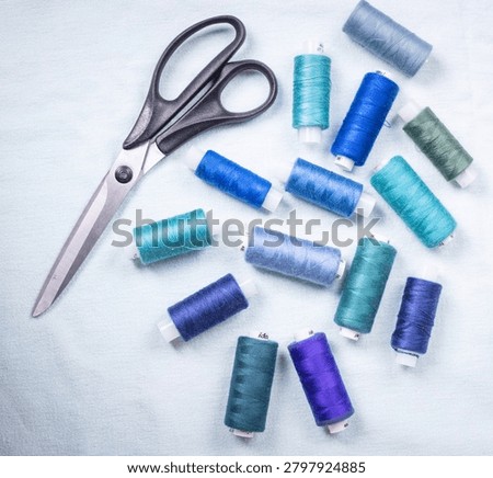 Scissors and blue thread spools on white surface, sewing, tools,