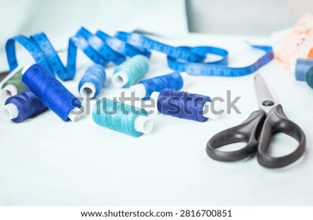 Scissors and blue thread spools on white surface, sewing, tools,