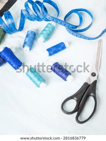 Scissors and blue thread spools on white surface, sewing, tools,