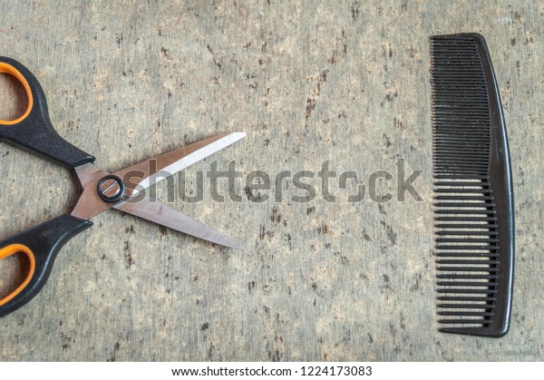 A scissors and a comb kept on a grey wooden textured\
table top view