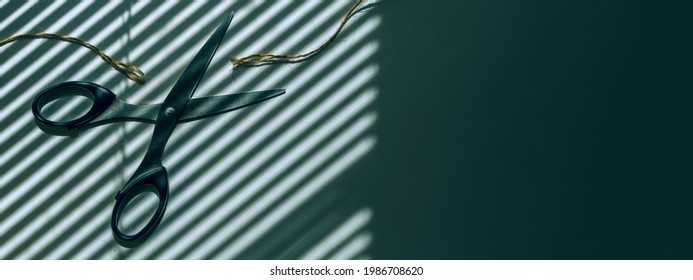 Scissors cut the thread. In the background is a shadow from the blinds. Place for text, hairdresser, office space on the windows of the blinds.