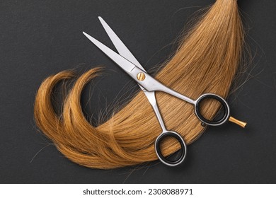 Scissors for cutting hair and a cut off strand of children's blond hair on a dark paper background