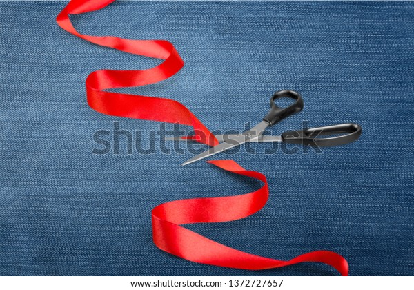Scissors cutting red ribbon, close-up view on\
blue background