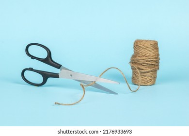 Scissors Cutting The Thread From The Coil On A Blue Background. Minimal Business Concept.