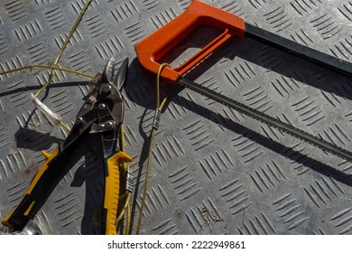 Scissors And A Hand-held Hacksaw Lie On A Metal Work Table. Concept Of Clipping Products Shopping Near A Hardware Store. Tied With Ropes From Kidnapping