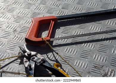 Scissors And A Hand-held Hacksaw Lie On A Metal Work Table. Concept Of Clipping Products Shopping Near A Hardware Store. Tied With Ropes From Kidnapping