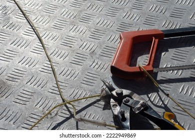 Scissors And A Hand-held Hacksaw Lie On A Metal Work Table. Concept Of Clipping Products Shopping Near A Hardware Store. Tied With Ropes From Kidnapping