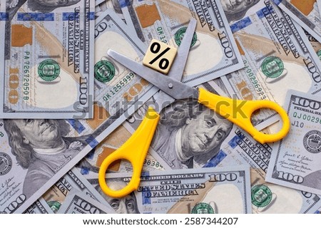 Scissors on a background of 100 dollar bills and a percent sign. The concept of interest rate cuts, the global world financial crisis, spending reductions.