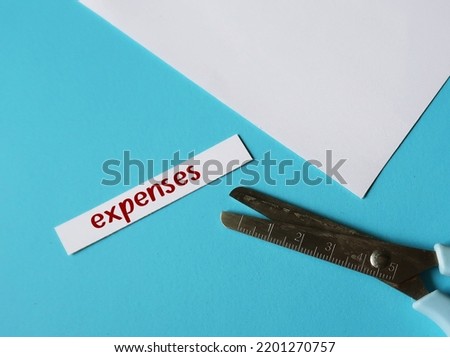 Scissors on blue background cutting paper piece with handwritten text EXPENSES, means to cut or reduce household or business expenses to regaining control of your financial budget