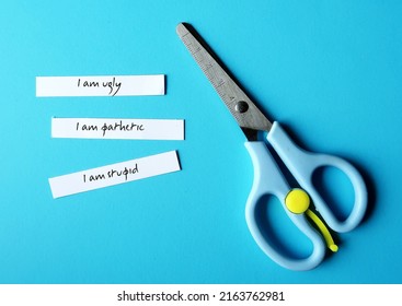 Scissors on blue background with text paper written I AM STUPID I AM UGLY I AM PATHETIC, concept of negative thoughts or self talk, harsh criticism inner voice critics caused by low self esteem