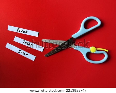 Scissors on red background, cut paper into pieces with handwritten text - Break Tasks Down - means to break down tasks into smaller parts which easier to work on, focus on doing one work at a time