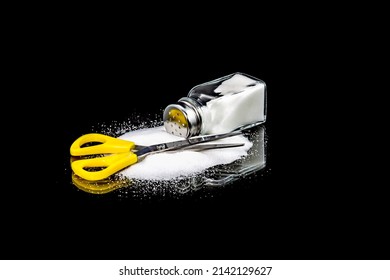 Scissors, salt shaker and spill salt on a black background. Symbol of cutting salt.