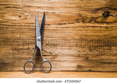 Scissors Sits Half Open On A Worn Butcher Block Counter Top. Vintage Aged Used Scissors Lie On Aged Wooden Table Background. Texture Backdrop. Empty Copy Space For Inscription Or Other Objects.