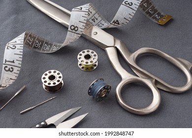 Scissors, spools of thread, needles, and a centimeter lie on the dark gray fabric of the T-shirt. Sewing accessories on the background of sewn clothes. Cutting and sewing concept. Tailor's Desk.
