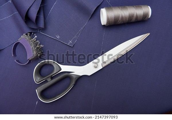 Scissors and tailor tools on blue fabric. Fabric\
cutting. Clothes sewing. Clothing repair. Tailoring. Close up view.\
Top view