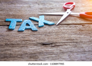 Scissors with text TAX on the rusty wooden background. A tax cut concept. Selective focus