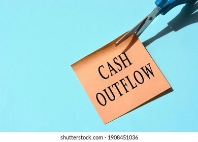 Scissors That Cut Yellow Notepad With Cash Outflow Text On A Blue Background. Cashflow Concept