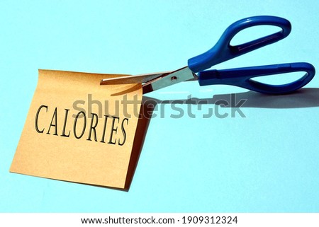 Scissors that cut yellow notepad with calories text on a blue background. Diet concept