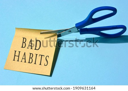 Scissors that cut yellow notepad with bad habits text on a blue background. Spending concept