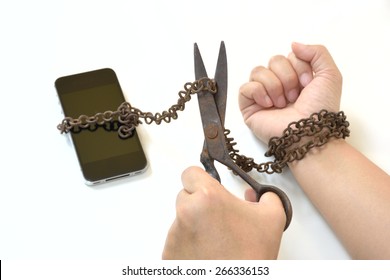 Scissors trying to cut rusty iron chain that ties together hand and smart phone in concept of breaking social media and internet addiction