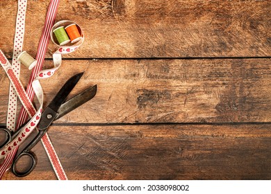scissors, vintage ribbons and spools of threads on brown wooden background 