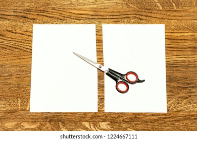 Scissors and a white sheet cut in half. Background yellowish brown wood.
