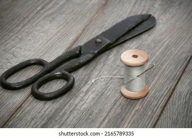 Scissors and a wooden spool of thread and needle. Old sewing tools on a wooden background, selective focus
