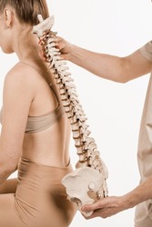 Scoliosis Is Sideways Curvature Of The Spine. Backbone Anatomical Model With Young Woman. Orthopedist Showing Spinal Column Model With Girl On White Background