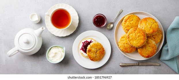 Scones, tea cakes with jam, clotted cream with tea. Traditional British teatime. Grey background. Top view.