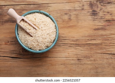 Scoop and bowl of brewer`s yeast flakes on wooden table, top view. Space for text