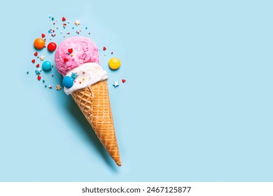 Scoop of vanilla and strawberry ice cream in wafer cone decorated with sugar sprinkles on blue background, copy space. Trendy creative layout of ice cream scoops.