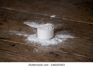 Scoop Of Whey Protein / Pre Workout Powder On A Wooden Table With Powder Spilled Next To The Scoop. Overfilled With Fitness Supplement.