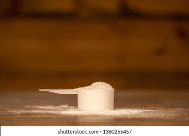 Scoop Of Whey Protein / Pre Workout Powder On A Wooden Table With Powder Spilled Next To The Scoop. Overfilled With Fitness Supplement.