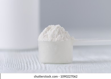 a scoop with white powder closeup and a jar on gray background