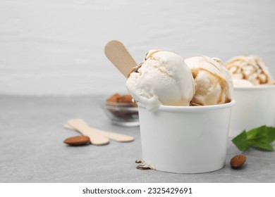 Sopas de helado con salsa de caramelo en un vaso de papel sobre mesa gris claro, cerrar. Espacio para texto