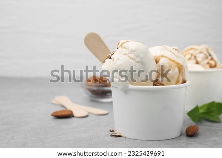 Scoops of ice cream with caramel sauce in paper cup on light grey table, closeup. Space for text