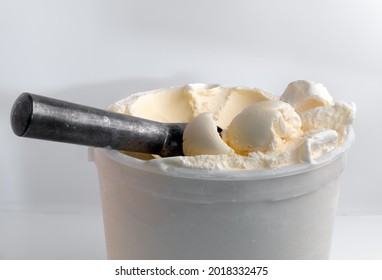 Scoops of vanilla ice cream on top of a tub filled with ice cream next to a metal scoop.