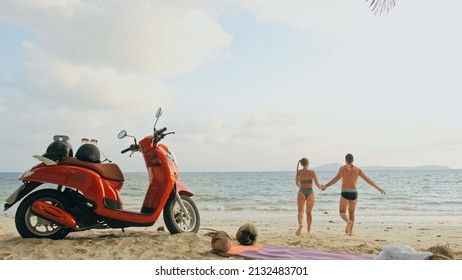 Scooter road trip. Lovely couple on red motorbike in white clothes on sand beach. Just married people kiss hugs walking near the tropical palm trees, sea. Wedding honeymoon by ocean. Motorcycle rent. - Powered by Shutterstock