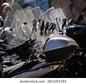 Scooters parked in a row, featuring windshields, handlebars, mirrors, and storage boxes, highlighting urban mobility