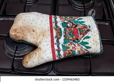 Scorched, Slightly Burnt Oven Mitt With Christmas Pattern Laying On Gas Oven Hob.