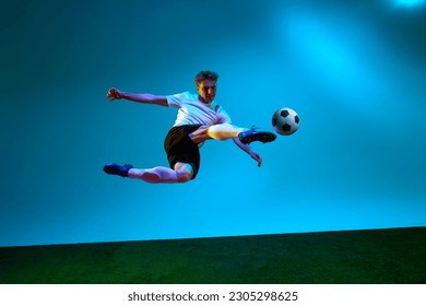 Scoring a goal. Professional man, football player in sports team uniform kicking the ball in motion over soccer field background in neon light. Active life, team game, sport, competition, ad concept - Powered by Shutterstock