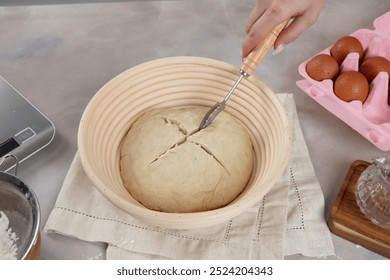 Scoring: The person is using a sharp tool to make cuts on the top of the dough.
Purpose: Scoring helps the bread to rise evenly and creates a distinctive crust pattern.