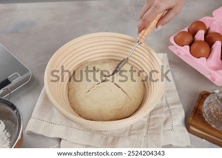 Scoring: The person is using a sharp tool to make cuts on the top of the dough.
Purpose: Scoring helps the bread to rise evenly and creates a distinctive crust pattern.