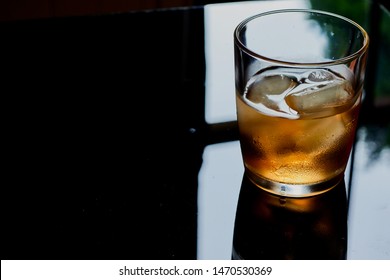 Scotch Whisky In A Glass With Ice Cubes,the Whisky Is On A Table, In A Dark Room  In Front Of A Window. 