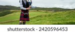 Scottish bagpiper in the Highlands of Scotland, panoramic mountains landscape background, UK