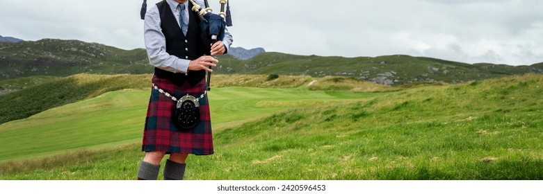 Scottish bagpiper in the Highlands of Scotland, panoramic mountains landscape background, UK