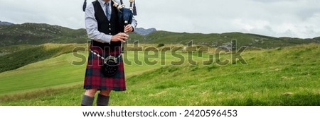 Scottish bagpiper in the Highlands of Scotland, panoramic mountains landscape background, UK
