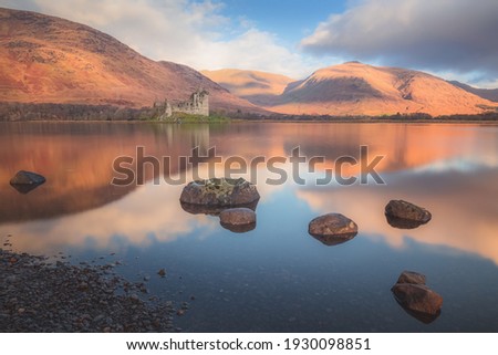Scottish Highlands landscape of the historic ruins of Kilchurn Castle reflected on a calm, peaceful Loch Awe with sunset or sunrise golden light.
